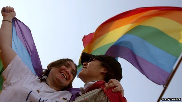A lesbian couple under a rainbow gay pride flag
