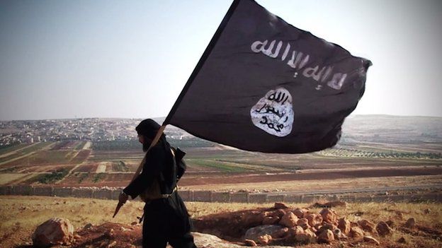 Islamic State militant carrying an IS flag, walking across a rocky landscape