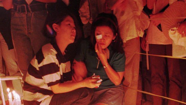 Two unidentified women pray in a makeshift altar during a mass in front of the gutted Ozone Disco March 25, 1996