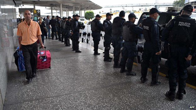 A traveller arrives at the departure terminal of Mexico City's international airport guarded by Federal Police personnel in riot gear on 20 November 2014.