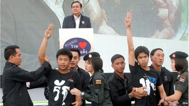 A photo made available on 20 November 2014 shows Thai students (front, 2-L and 3-R) being arrested by police officers and security guards as they flash anti-coup sign in front of Prime Minister Prayut Chan-ocha (back) while delivering a speech during his visit in Khon Kaen province, north eastern Thailand, 19 November 2014