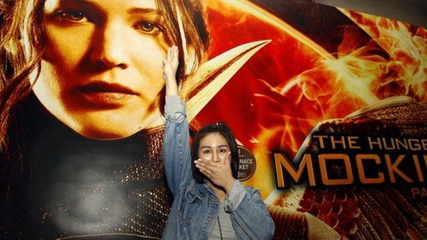Thai pro-democracy activist Nacha Kong-udom closes her mouth and flashes a three-finger salute in front of a poster of The Hunger Games movie at a cinema in Bangkok, Thailand, 20 November 2014