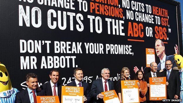 Ministers and Senators pose for media in front of a billboard showing an image of Prime Minister Tony Abbott at a ABC protest rally outside of Parliament House on 13 May 2014 in Canberra,