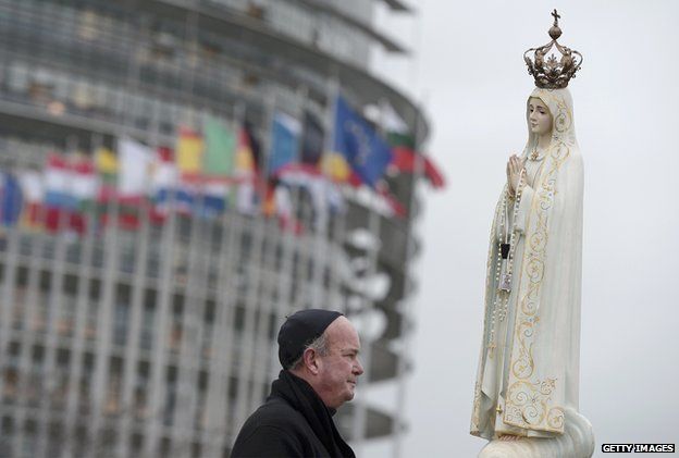 A cleric stands near a statue of the Virgin Mary in front the European Parliament building in Strasbourg, France, on 24 November 2014