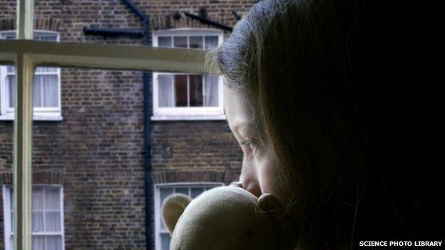 Anonymous child looking out of a window holding a teddy bear
