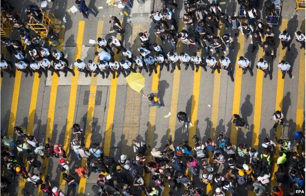 A lone pro-democracy demonstrator (C) carries a yellow umbrella in front of a line of policemen in Mongkok, Hong Kong, China, 26 November 2014.