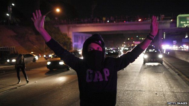 A man is illuminated by the lights of approaching police vehicles as protesters set up barricades and shut down the 101 freeway in Los Angeles, California, 25 November 2014