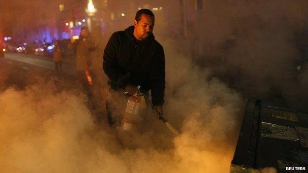 A local resident attempts to extinguish a street fire set by protesters in Oakland, California, 25 November 2014