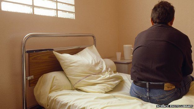 A man sits on his bed in a mental health ward