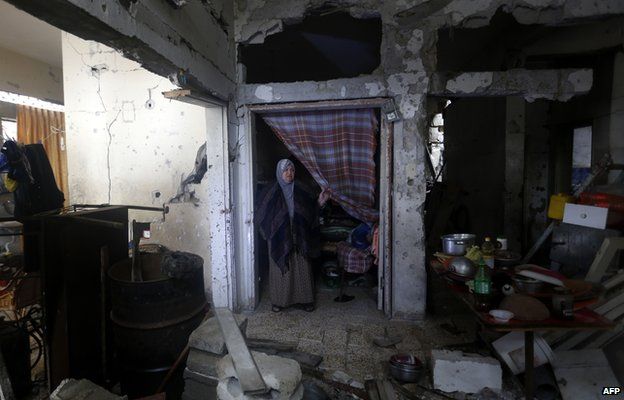 Palestinian woman stands in her destroyed home where she lives with her family on a rainy day in Gaza City's Shejaiya neighbourhood on 24 November 2014