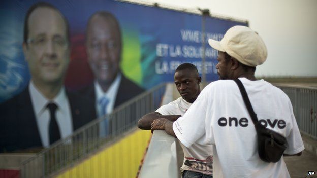 Two Guinean men stand on a pedestrian overpass near the People's Palace where a giant billboard featuring French President Francois Hollande and his Guinean counterpart Alpha Conde is displayed in Conakry, Guinea, 26 November 2014