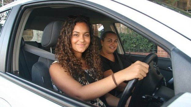 Two smiling Aboriginal women in front seats of white car