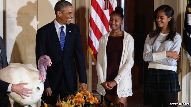 US President Barack Obama smiles at his daughters Sasha and Malia after he pardoned a turkey during a ceremony at the White House on 26 November 2014 in Washington