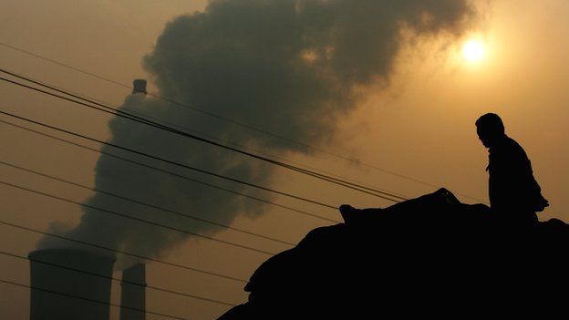A Chinese man squats on a truck near a power plant emitting plumes of smoke from industrial chimneys on 30 October 2007 in Beijing, China.