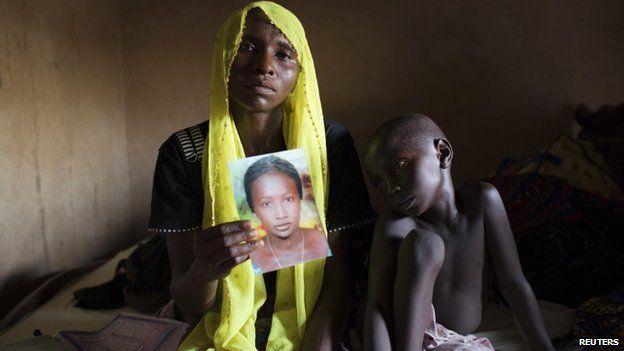 Rachel Daniel, 35, holds up a picture of her abducted daughter Rose Daniel, 17, as her son Bukar, 7, sits beside her at her home in Maiduguri , Nigeria on 21 May 2014