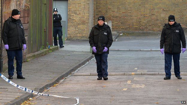 Police officers search an area where Joel Adesina was stabbed
