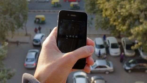 The Uber smartphone app, used to book taxis using its service, is pictured over a parking lot as auto-rickshaws (background) ply a road in the Indian capital New Delhi on December 7, 2014