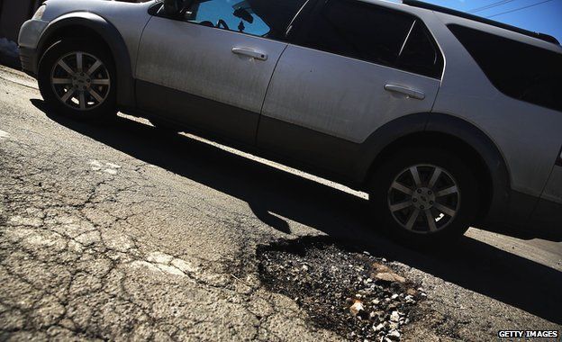 A car drives past a pothole