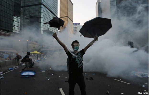 A protester (C) raises his umbrellas in front of tear gas which was fired by riot police to disperse protesters blocking the main street to the financial Central district outside the government headquarters in Hong Kong, 28 September 2014.