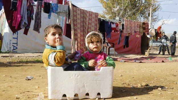 Syrian refugee children sit in a box at a makeshift settlement in Qab Elias in the Bekaa valley