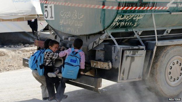 Syrian children hitch a ride from the back of a water tanker at the Al Zaatari refugee camp in the Jordanian city of Mafraq (7 December 2014)