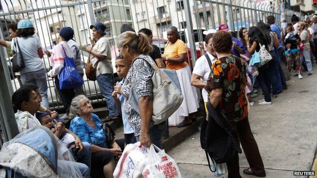 People stand in line to buy goods outside a supermarket in Caracas , Venezuela (10 December 2014)