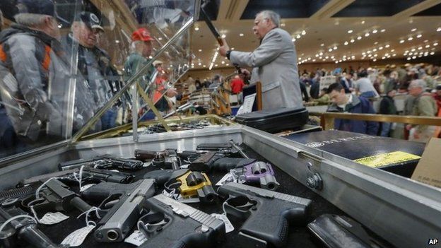 In this 26 January, 2013 file photo, handguns appear on display at the table of David Petronis of Mechanicville, NY, standing with rifle.