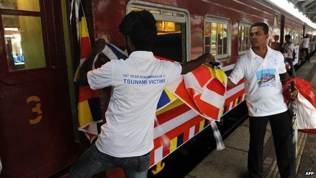 Sri Lankan railway employees place flags on a train compartment that was swept away during the 2004 tsunami and later retrieved and restored, as the Ocean Queen Express prepares to set off from the Colombo Fort railway station in Colombo on December 26, 2014