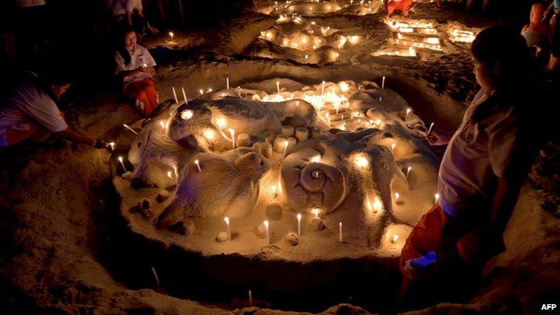 Thai students place candles on a sand sculpture during commemorations on the the tenth anniversary of the 2004 tsunami at Patong beach in Phuket province on December 26, 2014