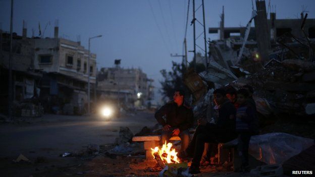 Palestinians warm themselves by a fire near the ruins of houses which witnesses said were destroyed by Israeli shelling during the most recent conflict between Israel and Hamas, in the east of Gaza City 1 December 2014.