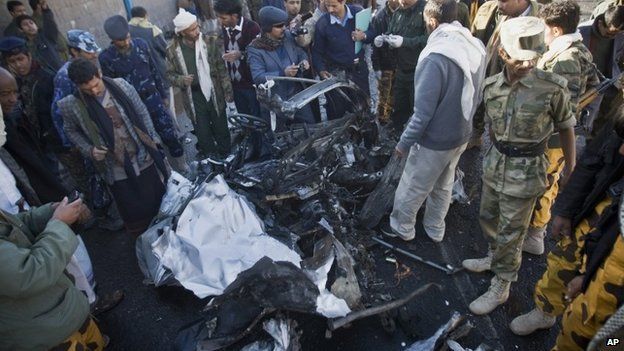 People inspect wreckage of car destroyed by bomb blast in Sanaa, Yemen (7 January 2015)