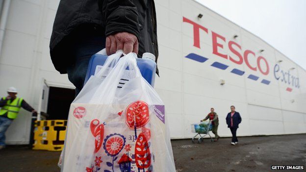 Man with Tesco bag walks past side of Tesco Extra store in Glasgow