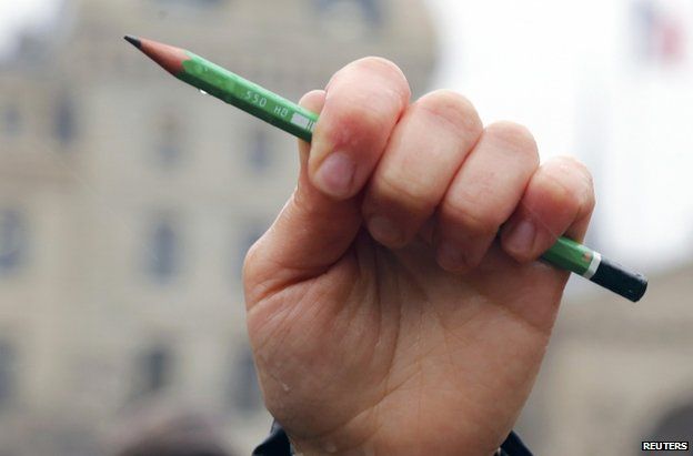 A person holds up a symbolic pencil in front of Notre Dame cathedral in Paris, 8 January