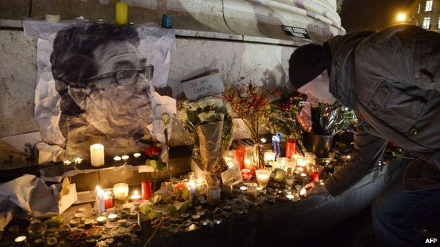 A man lights a candle next to a picture of late French cartoonist Tignous during a rally at Republic Square in Paris on 8 January 2015,