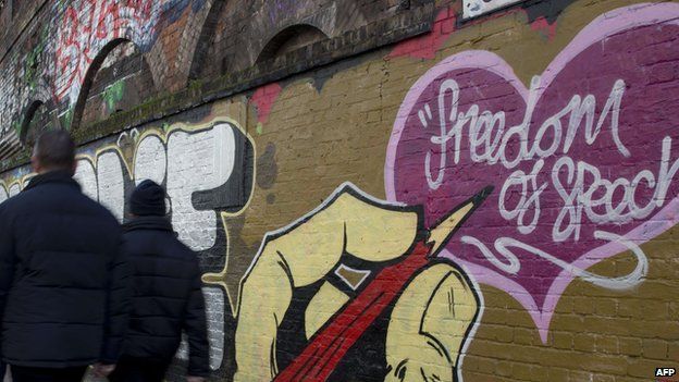 Pedestrians in London walk past a wall with freedom of speech scrawled on it
