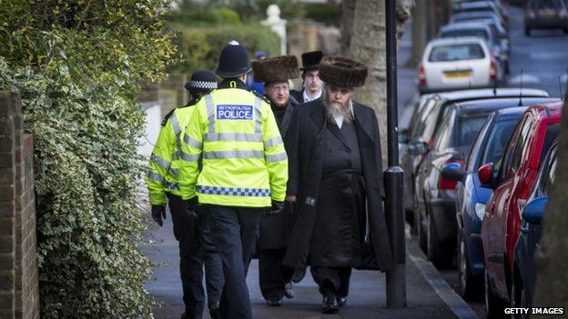 Police carry out a patrol as Jewish men walk past