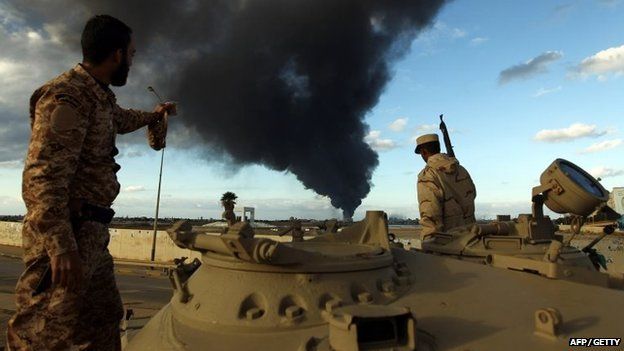 Members of the Libyan army stand on a tank as heavy black smoke rises after clashes against Islamist gunmen in the eastern Libyan city of Benghazi