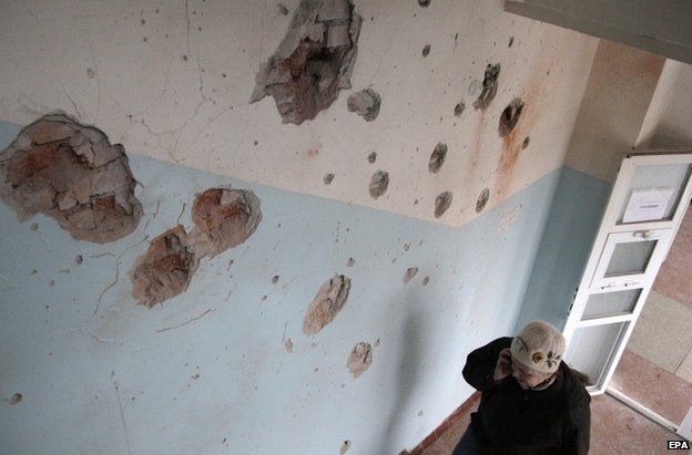 A woman walks past a wall pocked with shrapnel at a hospital in the city of Donetsk, 20 January