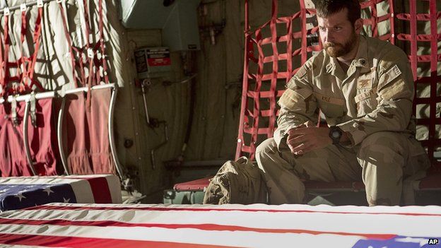 Chris Kyle, played by Bradley Cooper, sits next to flag-draped coffins in the film American Sniper