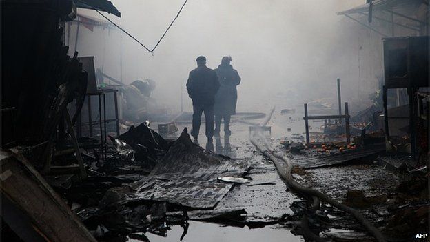 People walk past burnt out kiosks at a street market close to a destroyed building housing the housing the local media known as the Press House, in central Grozny, on December 4, 2014