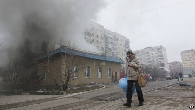 A woman resident passes by a burning house in Mariupol, Ukraine on 24 January 2015