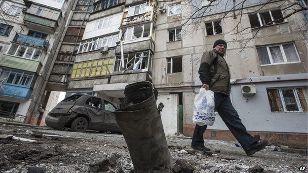 A man walks by a burned car and a piece of exploded Grad missile, outside an apartment building in Vostochniy district of Mariupol, Eastern Ukraine, Sunday, Jan. 25, 2015