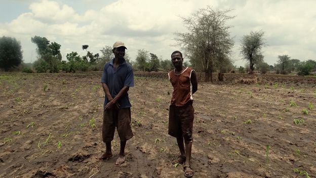 Two farmers stand in flood-damaged field