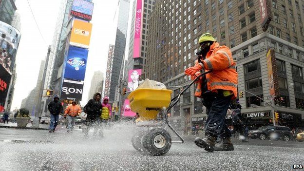 A worker spreads salt on the sidewalk in Times Square in preparation for a large winter storm in New York, New York, USA, 26 January 2015