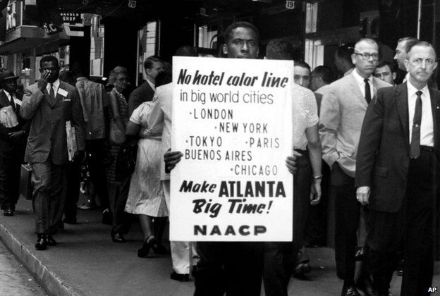 Man protesting and holding a sign reading: "No hotel color line"