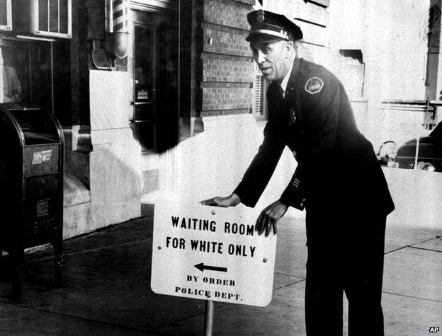 Policeman with a sign reading: "Waiting room for white only by order police dept."