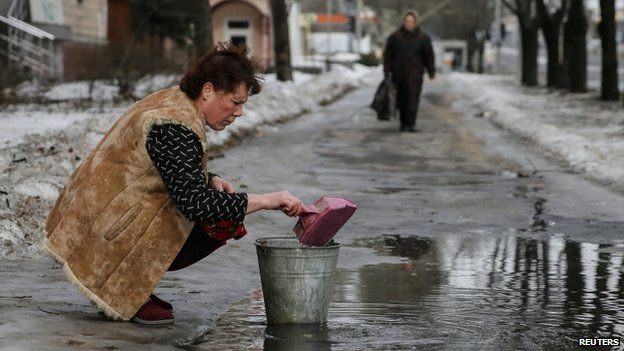 A woman gathers water from a puddle into a bucket in Donetsk. Photo: 31 January 2015