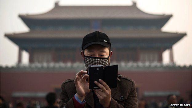 A Chinese man wears a mask to protect against pollution as he uses his smartphone on a hazy day outside the Forbidden City 20 November 2014 in Beijing, China