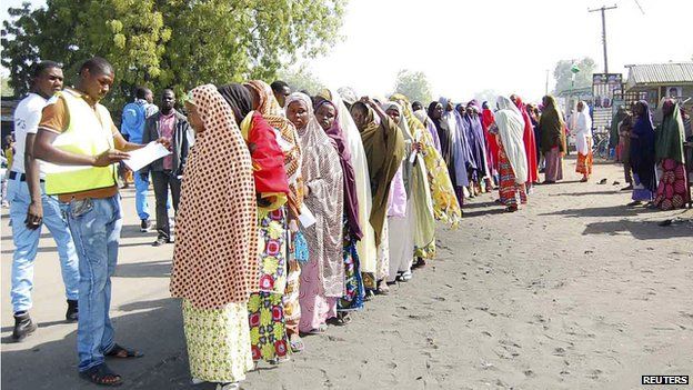 Displaced people fleeing from violence wait in line to receive relief materials at a camp for displaced people camp in Borno State