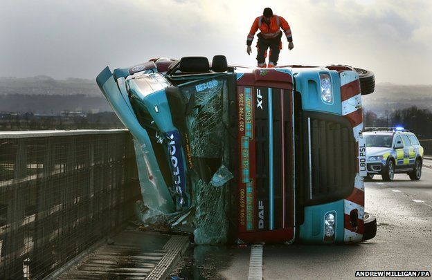 A man climbs on a lorry on its side after being blown over in strong winds on the Clackmannanshire Bridge over the Firth of Forth, Scotland